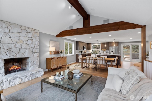 living area featuring beamed ceiling, high vaulted ceiling, a stone fireplace, light wood finished floors, and baseboards