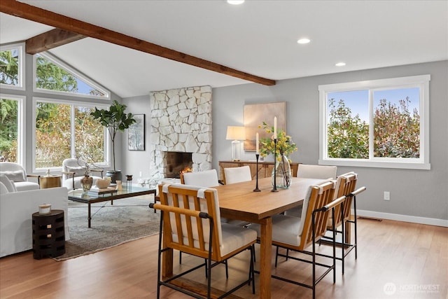 dining area featuring lofted ceiling with beams, baseboards, light wood-style floors, and a stone fireplace