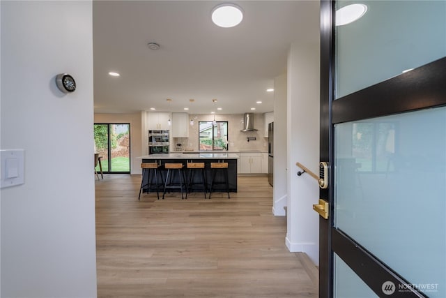 kitchen featuring a kitchen breakfast bar, a center island, white cabinetry, wall chimney exhaust hood, and light countertops