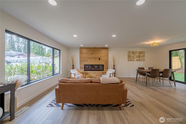 living area with a wealth of natural light, light wood-type flooring, a large fireplace, and visible vents