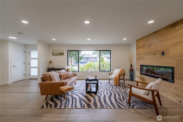 living room with a glass covered fireplace, recessed lighting, wood finished floors, and wood walls