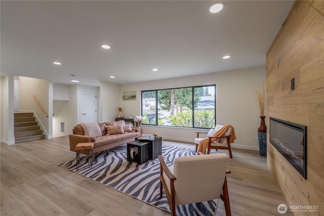 living room featuring baseboards, recessed lighting, a fireplace, stairs, and light wood-style floors