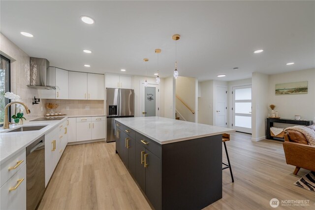 kitchen featuring wall chimney range hood, light wood-style flooring, appliances with stainless steel finishes, white cabinetry, and a sink