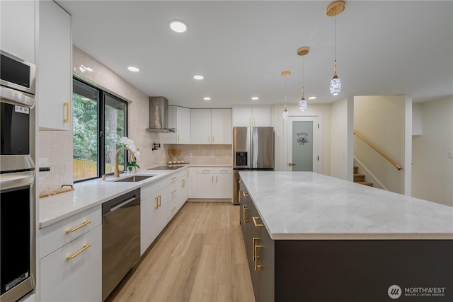 kitchen featuring a sink, white cabinets, appliances with stainless steel finishes, wall chimney range hood, and tasteful backsplash