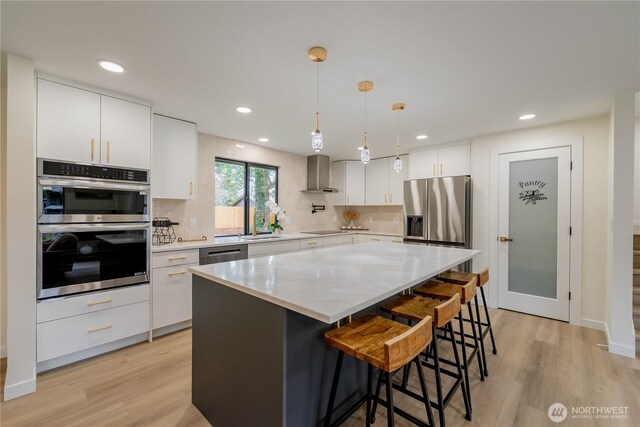 kitchen featuring white cabinetry, stainless steel appliances, light wood-style floors, and wall chimney range hood