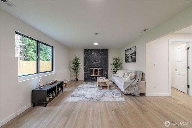 living area with visible vents, baseboards, light wood-style floors, and a premium fireplace