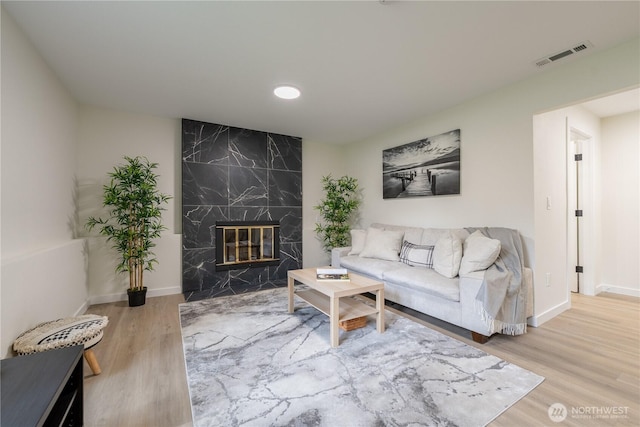 living area featuring a fireplace, wood finished floors, visible vents, and baseboards