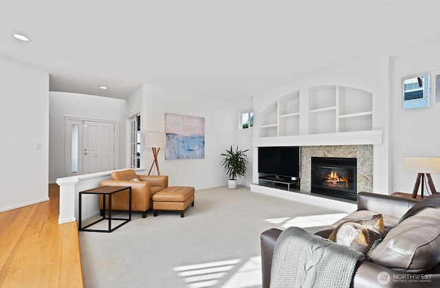 living room with built in shelves, plenty of natural light, recessed lighting, wood finished floors, and a glass covered fireplace