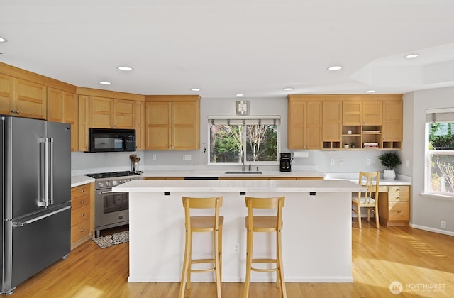 kitchen featuring a kitchen island, light countertops, premium appliances, light wood-style flooring, and a sink