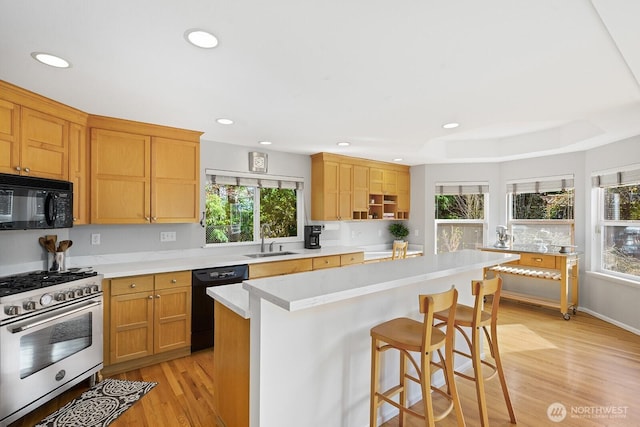 kitchen with a breakfast bar, black appliances, light countertops, and light wood-type flooring