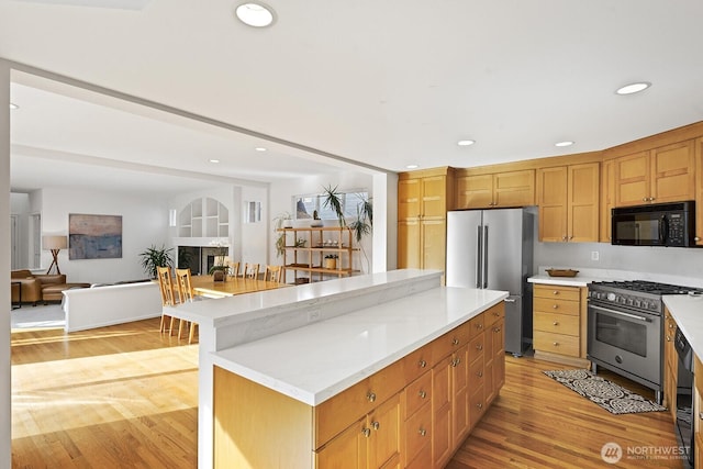 kitchen featuring open floor plan, stainless steel appliances, light wood-style floors, a fireplace, and light countertops