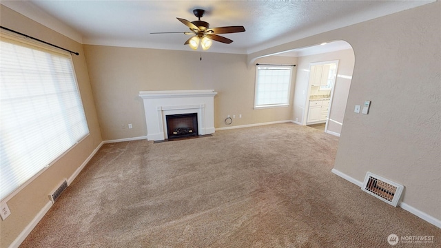 unfurnished living room with a fireplace with flush hearth, arched walkways, visible vents, and carpet floors