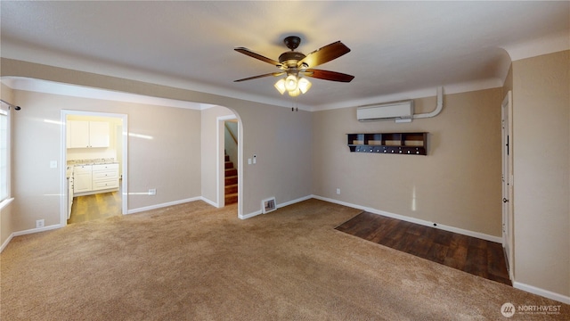 empty room featuring a wall mounted AC, carpet floors, arched walkways, ceiling fan, and stairs