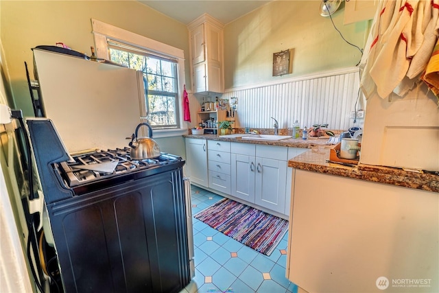 kitchen featuring tile patterned floors, white cabinets, black range with gas stovetop, and a sink