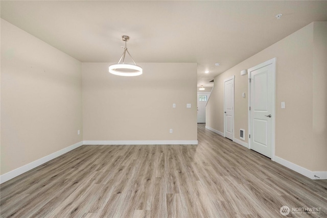 empty room with light wood-style flooring, visible vents, and baseboards