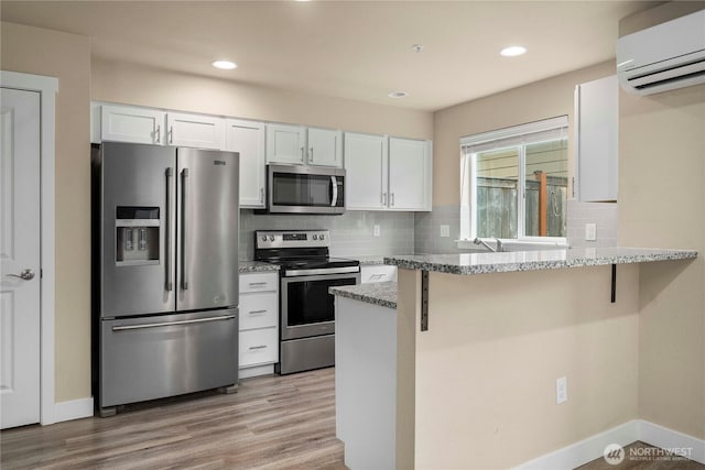 kitchen with decorative backsplash, white cabinets, light wood-style floors, a wall mounted air conditioner, and appliances with stainless steel finishes