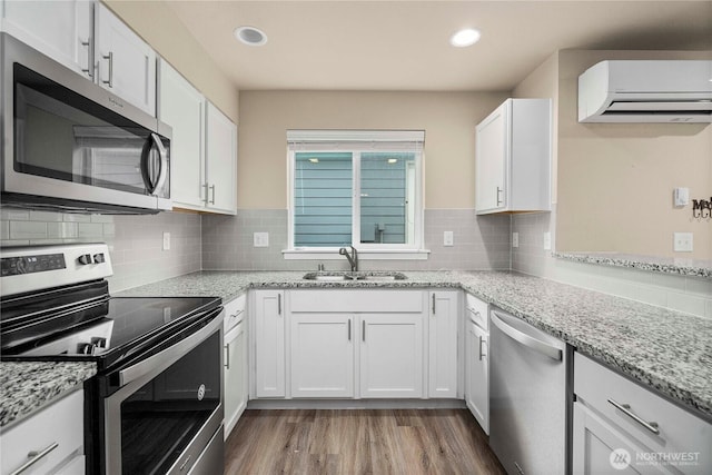 kitchen with a wall unit AC, stainless steel appliances, wood finished floors, white cabinetry, and a sink