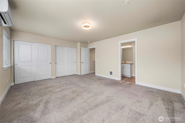 unfurnished bedroom with baseboards, carpet, a wall mounted AC, and multiple closets