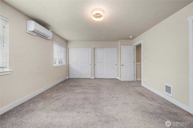 unfurnished bedroom with visible vents, multiple closets, an AC wall unit, carpet flooring, and baseboards