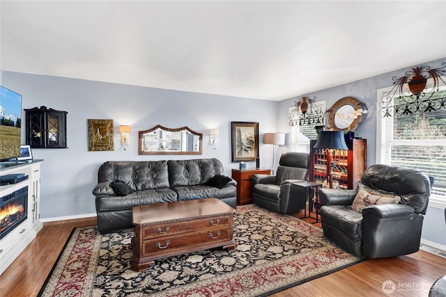 living room featuring a glass covered fireplace, visible vents, baseboards, and hardwood / wood-style floors