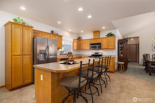 kitchen with a kitchen island, light countertops, appliances with stainless steel finishes, a kitchen breakfast bar, and a sink