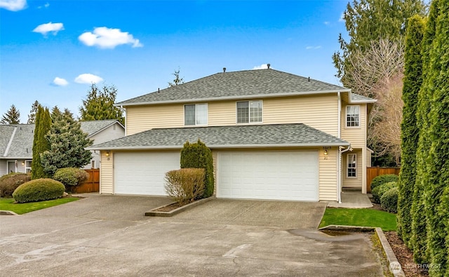 traditional-style house featuring a garage, roof with shingles, concrete driveway, and fence