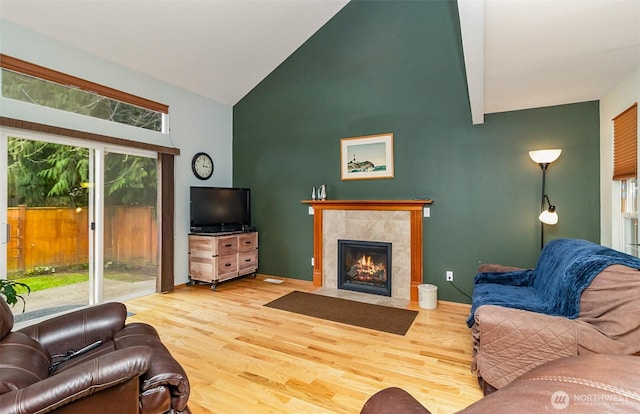 living area with wood finished floors, high vaulted ceiling, a healthy amount of sunlight, and a tile fireplace