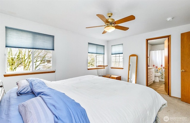 bedroom with baseboards, light colored carpet, ensuite bath, and a ceiling fan