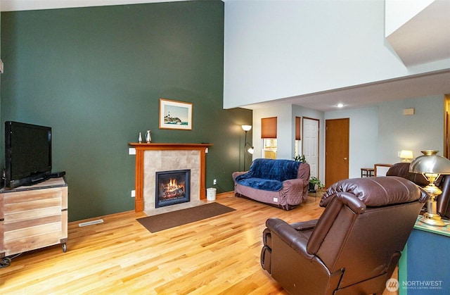 living area with visible vents, a tile fireplace, a high ceiling, and wood finished floors