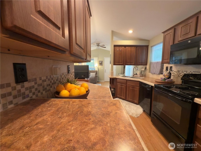 kitchen with a sink, decorative backsplash, black appliances, light countertops, and light wood-type flooring