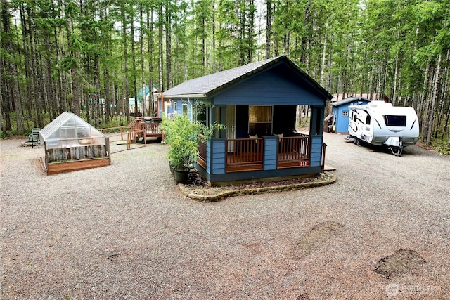 view of front of house with a greenhouse, a forest view, and an outbuilding