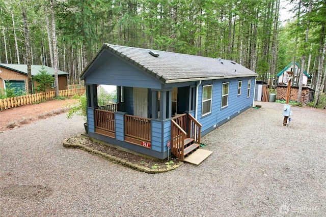 view of front facade with covered porch, gravel driveway, a wooded view, and a tile roof