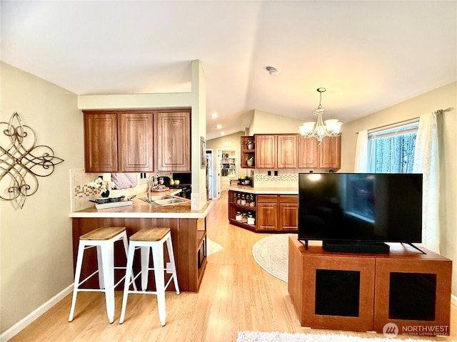 kitchen with backsplash, open shelves, brown cabinets, a kitchen breakfast bar, and a sink