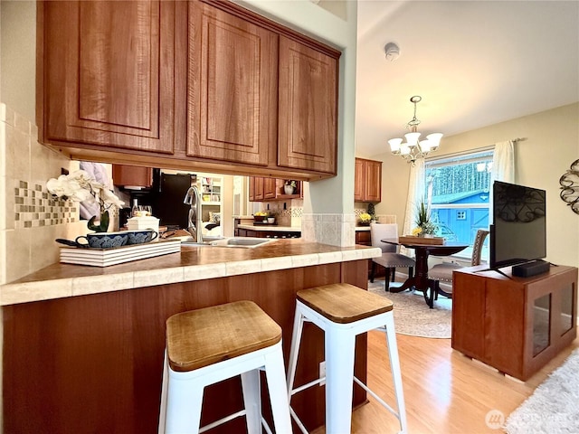 kitchen featuring a breakfast bar area, decorative backsplash, brown cabinets, light wood-style flooring, and an inviting chandelier