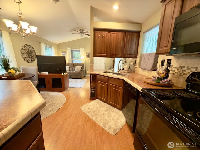 kitchen featuring light countertops, vaulted ceiling, light wood-style flooring, black appliances, and a sink