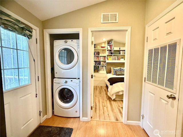 laundry area with a heating unit, stacked washer and dryer, visible vents, and light wood finished floors