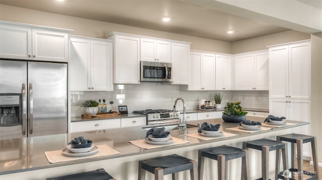 kitchen with tasteful backsplash, white cabinets, stainless steel appliances, and a breakfast bar area