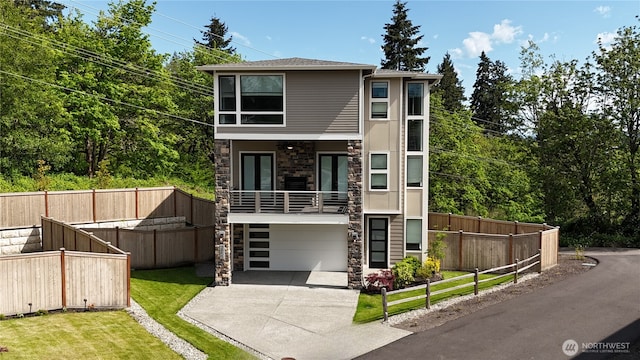 contemporary house with stone siding, an attached garage, a front yard, a balcony, and driveway