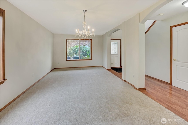 empty room with arched walkways, an inviting chandelier, light wood-style flooring, and baseboards