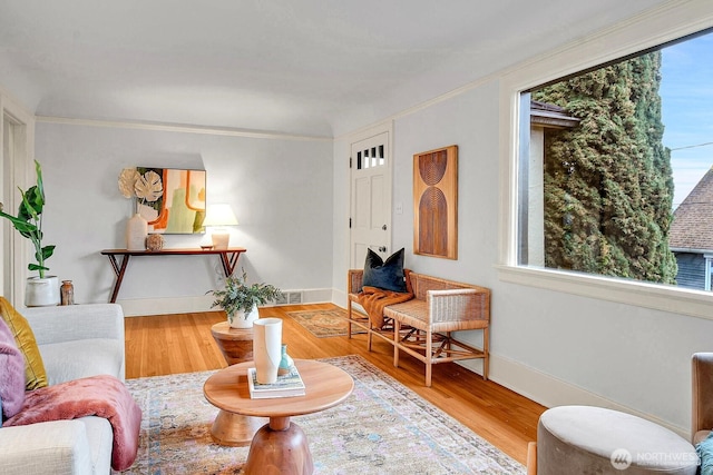 living area with visible vents, baseboards, wood finished floors, and ornamental molding