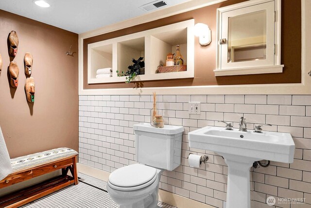 half bath featuring tile patterned floors, visible vents, toilet, a sink, and tile walls