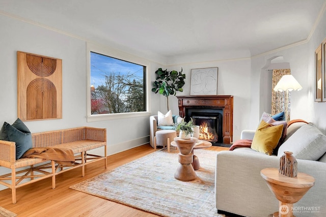 living area with a fireplace with flush hearth, crown molding, and wood finished floors