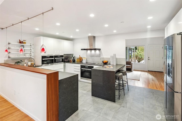 kitchen featuring a sink, a peninsula, appliances with stainless steel finishes, wall chimney exhaust hood, and white cabinets