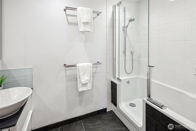 bathroom featuring tile patterned flooring, tiled shower, baseboards, and a sink