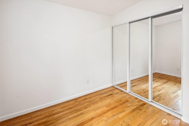 unfurnished bedroom with wood finished floors, baseboards, and a closet