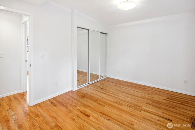 unfurnished bedroom with a closet, baseboards, light wood-style floors, and visible vents