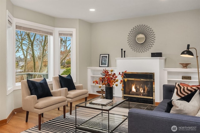 living area featuring a glass covered fireplace, recessed lighting, baseboards, and wood finished floors