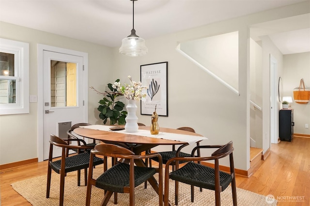 dining room with light wood-type flooring, baseboards, and stairs