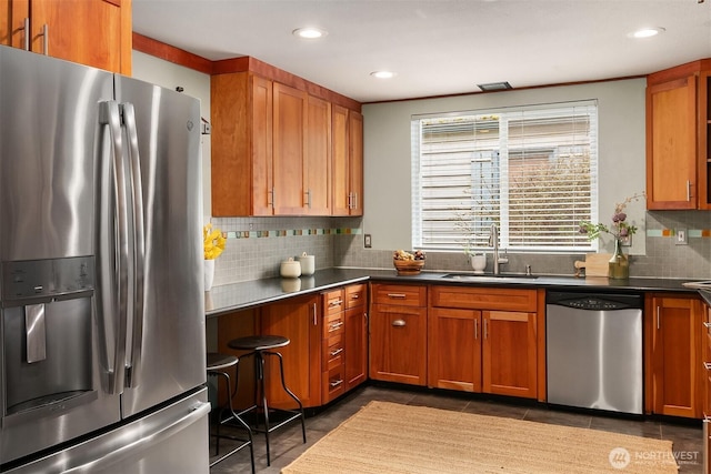 kitchen with backsplash, dark tile patterned floors, brown cabinets, appliances with stainless steel finishes, and a sink