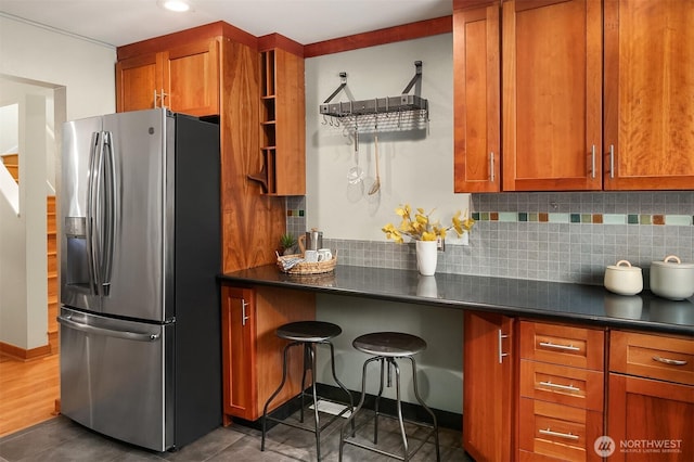 kitchen featuring dark countertops, brown cabinets, stainless steel refrigerator with ice dispenser, and backsplash